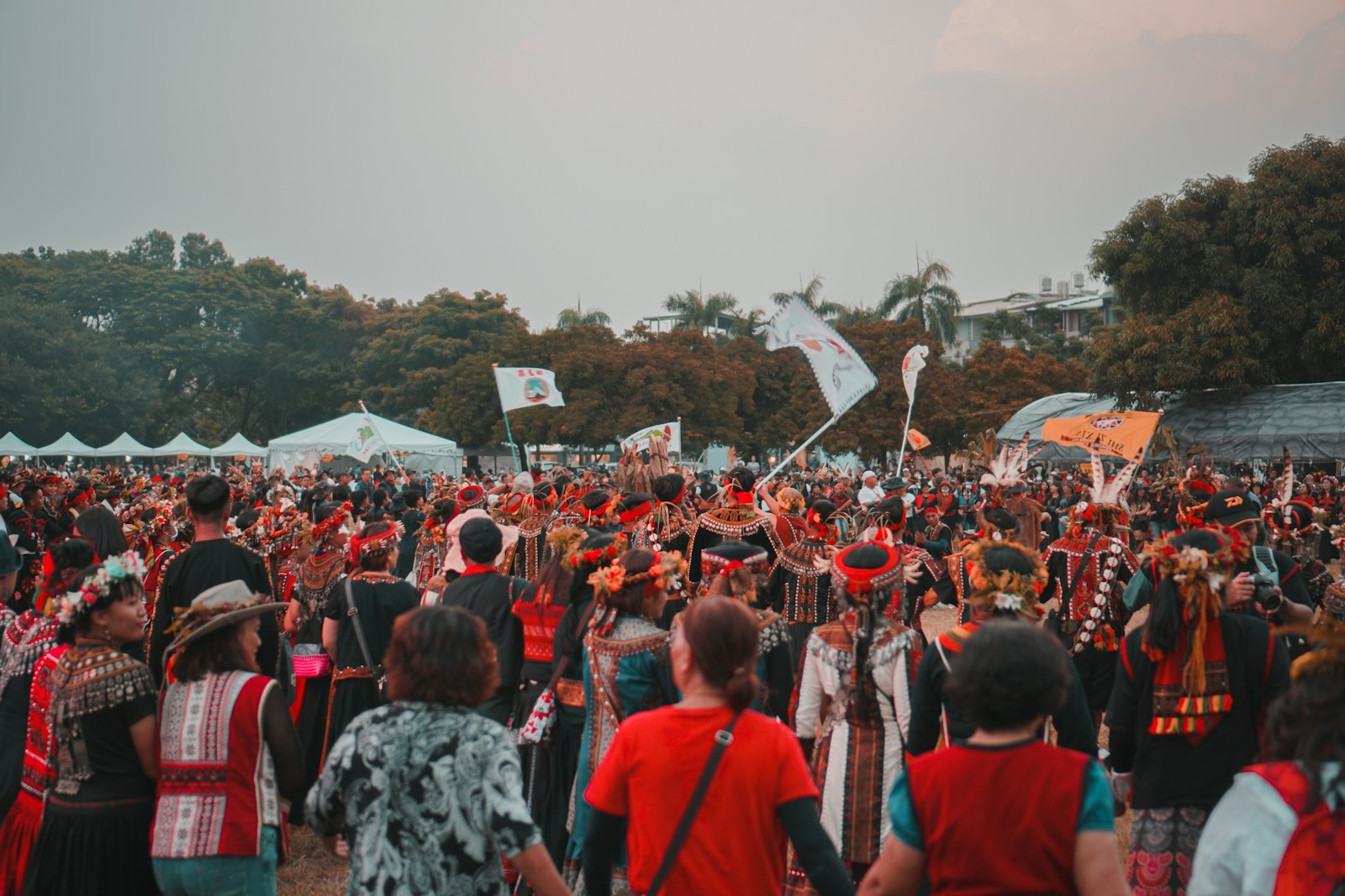 A wide-angle view of a music festival main stage at golden hour with a small group of professional photographers in dark clothing visible in the photo pit at the front, silhouetted against the bright stage and a vast crowd behind.