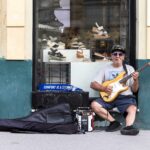 Musicista con chitarra e una piccola cassa amplificata su una via lastricata del centro