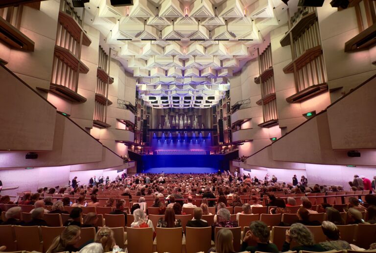Interno di una sala da concerto con palco illuminato e file di posti a sedere vuoti